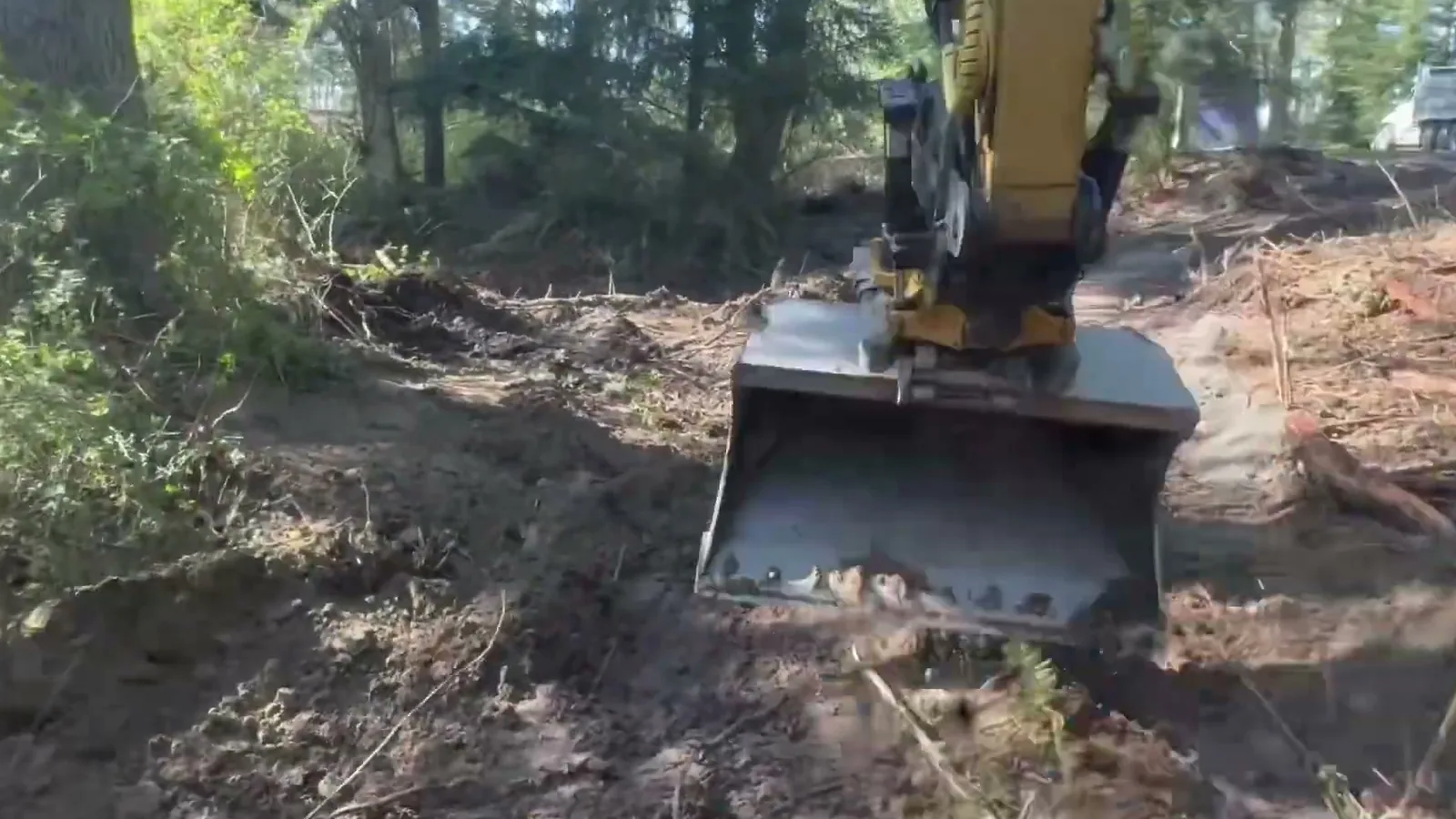 Excavator bucket digging into the ground on a wooded lot