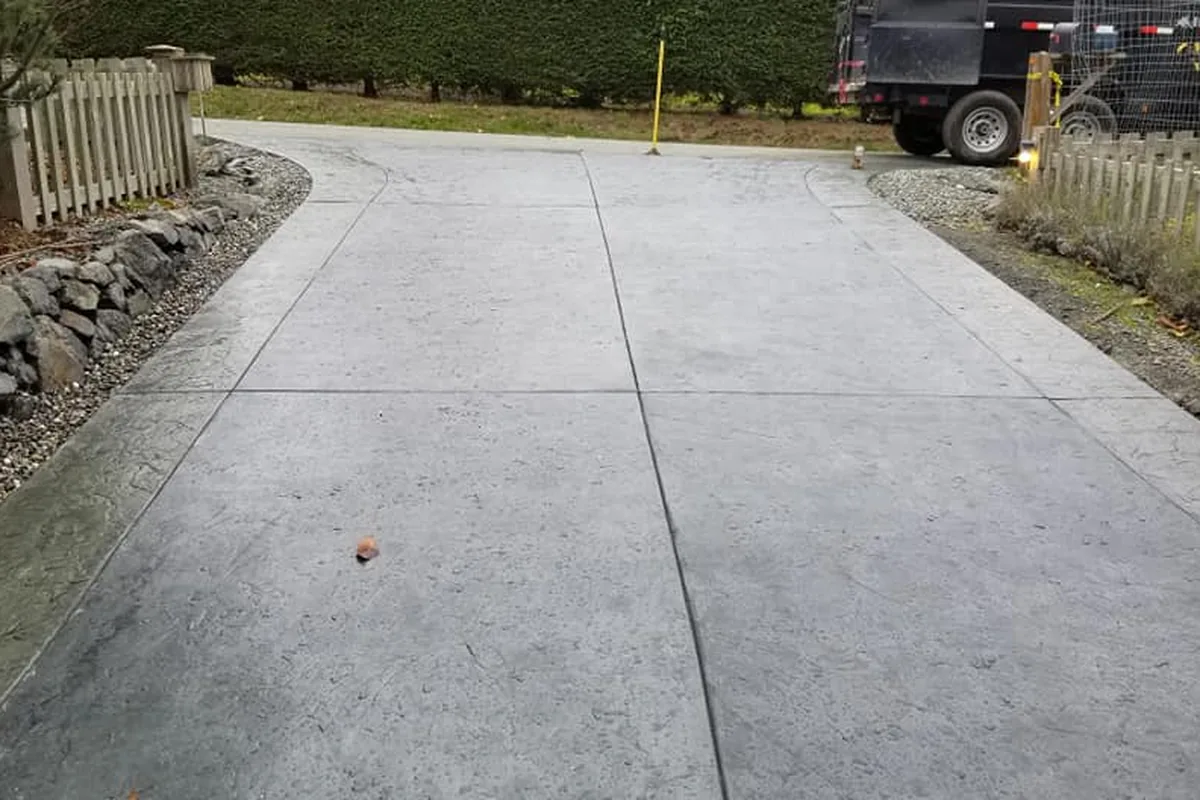 New concrete driveway with a textured border band and tooled control joints, a dump trailer parked at the far end