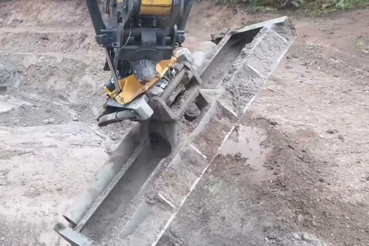 Excavator running a roller compactor along a footing trench on a graded building pad