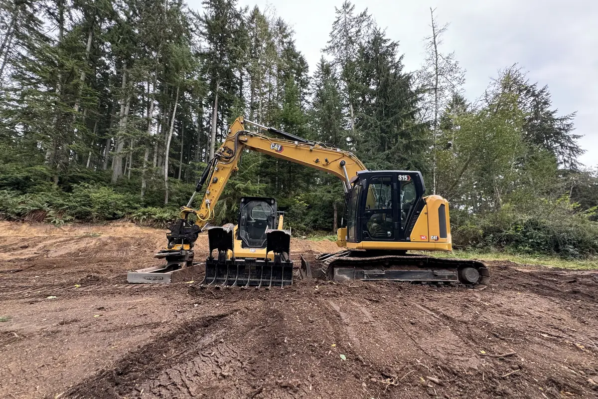 A CAT 315 excavator and a compact track loader on freshly cleared ground at the edge of the woods