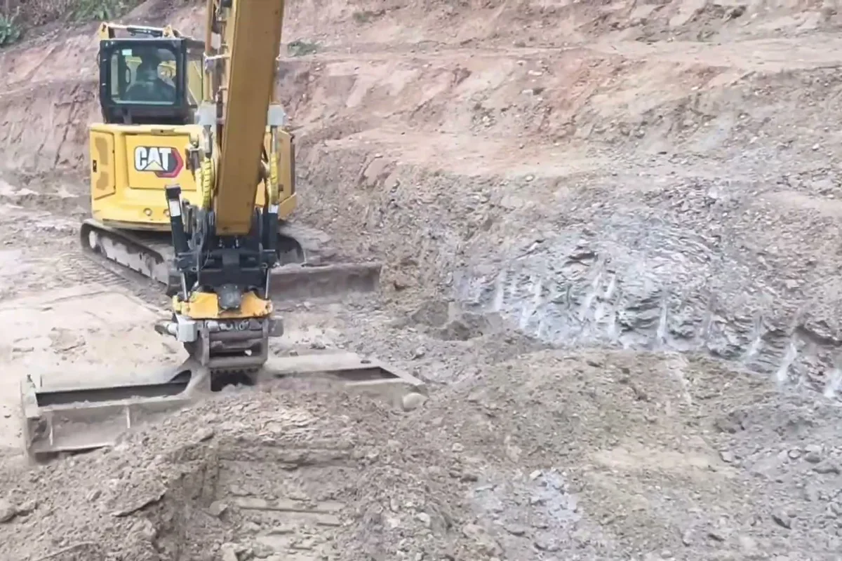 Mini excavator leveling a cut bench below a slope before wall construction